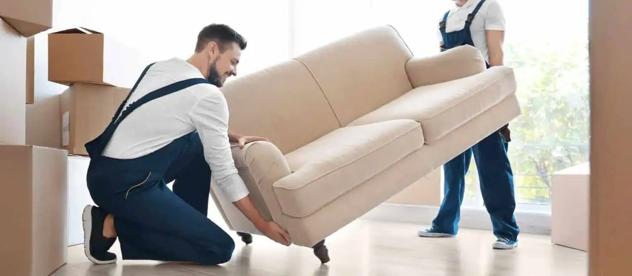 Professional movers using straps to safely lift and transport heavy furniture.