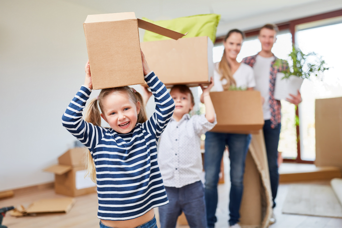 Children carrying moving boxes with parents during a home move.